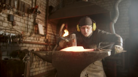 Blacksmith making a knife with a hammer on the forge.