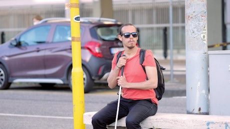 Blind man waiting on a bench at traffic lights.