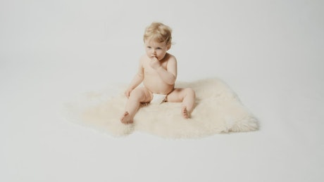 Blonde baby in diaper sits on furry rug
