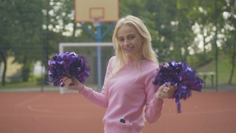Blonde cheerleader shaking purple pom poms.