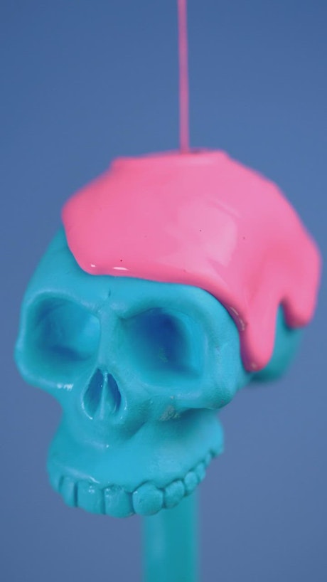 Blue plastic skull covered with a pink liquid on a blue background.