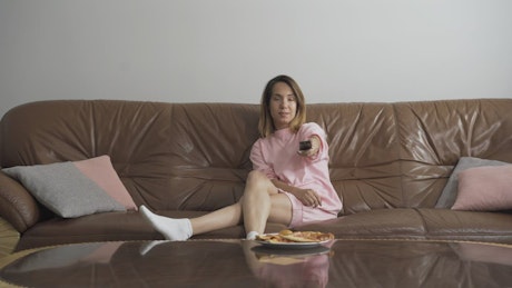 Bored woman flips TV channels on sofa with remote