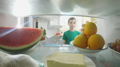 Boy and sister open the refrigerator to take two oranges.