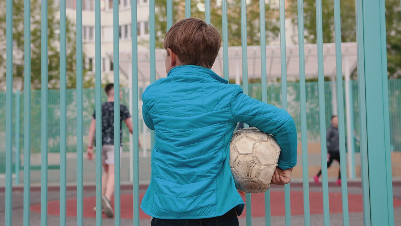 Boy holding deflated ball watching other kids playing football - Mixkit