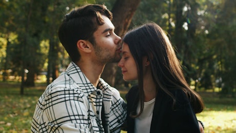 Boyfriend kissing his partner on the head in the park.