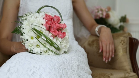 Bride sitting on a couch with a bouquet of white and pink flowers.