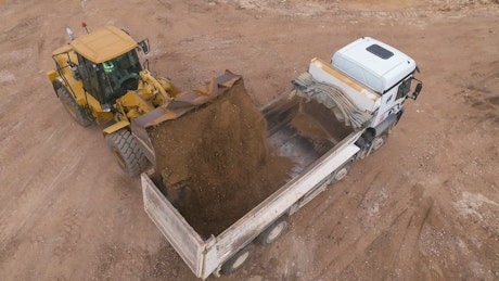 Bucket loader pouring dirt into a truck.
