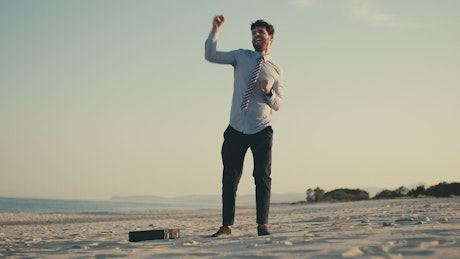 Businessman breaks free from work and dances on the beach.