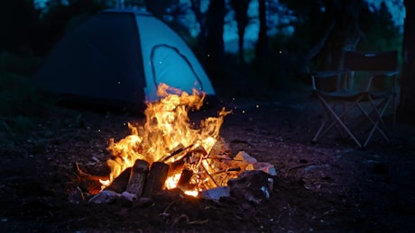 Campfire burning at night with a tent in the background.