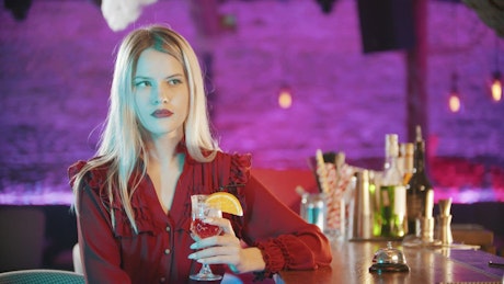 Captivating woman with a drink at a bar counter.