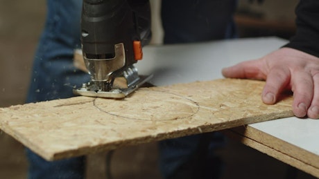 Carpenter uses a jigsaw to cut a perfect circle in a plank of wood.