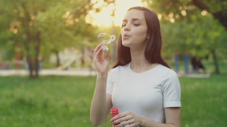 Cheerful girl blowing soap bubbles in a park