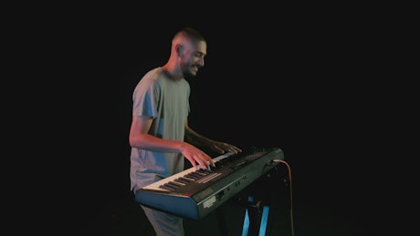 Cheerful pianist playing a keyboard in a dark place.