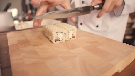 Chef chopping a roll of sushi with a sharp knife.
