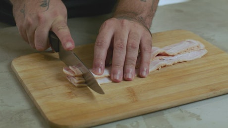 Chef chopping bacon on a board.