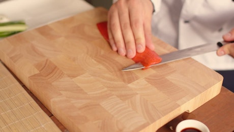 Chef cutting a piece of fresh salmon with a sharp knife.