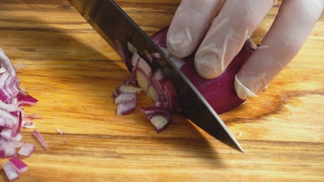 Chef cutting onion with gloves.