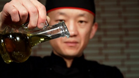 Chef pouring sesame oil from a glass bottle.