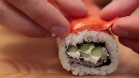 Chef removing a slice of salmon from a roll of sushi.