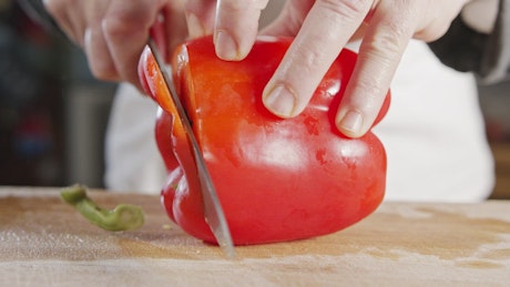 Chef slicing a red bell pepper on a wooden chopping board.