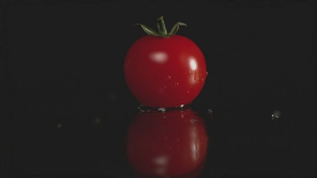 Cherry tomato falling onto a wet surface against a black background.