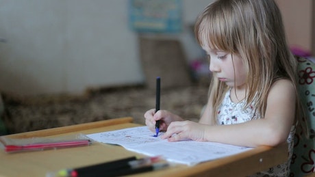 Child colouring in her book with pencils.