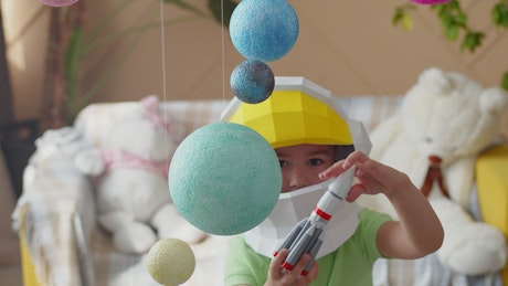 Child dressed as an astronaut plays with a toy spaceship.