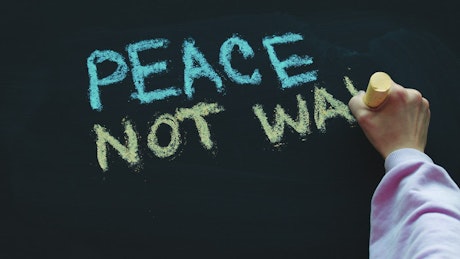 Child hand writes 'Peace Not War' on blackboard.