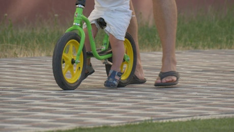 Child on a bicycle with his dad behind
