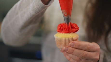 Close up of a cupcake being decorated with orange icing.