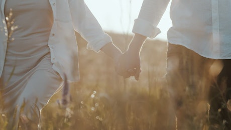 Close up of a happy couple walking through a field hand in hand.