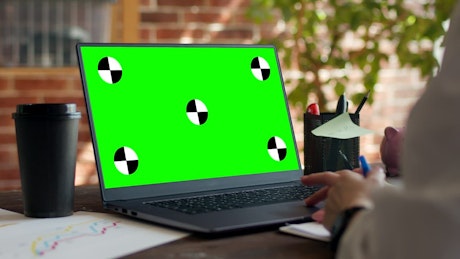 Close up of a laptop with green screen sitting on a desk.