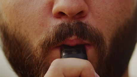 Close up of a man inhaling a vape.