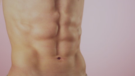Close up of a mans abs against a pink background.