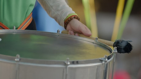 Close up of a musician tapping a rhythm on a hanging drum.