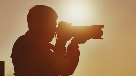 Close up of a professional photographer taking a picture of a sunset.