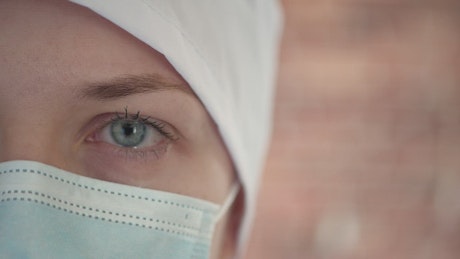 Close up of a struggling nurse in a mask blinking back tears.