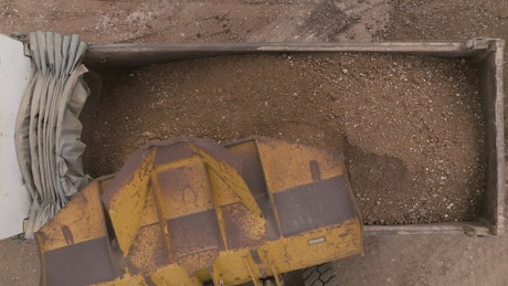 Close up of a truck emptying dirt into a truck.