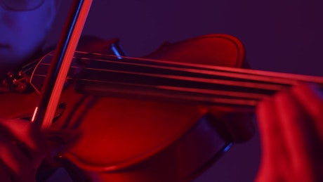 Close up of a violinist expertly playing a violin against a red light.