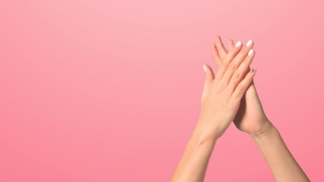 Close up of hands clapping against a pink background.