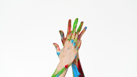 Close up of hands covered in paint against a white background.