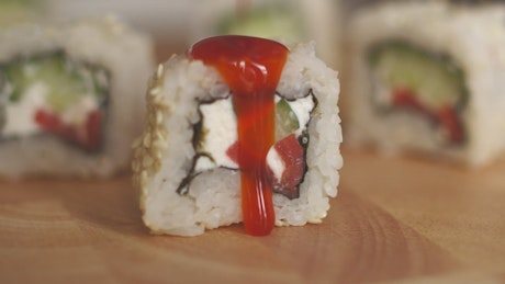 Close up of sauce being poured onto a slice of sushi.