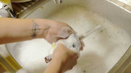 Close up of someone washing dishes in a soapy sink.