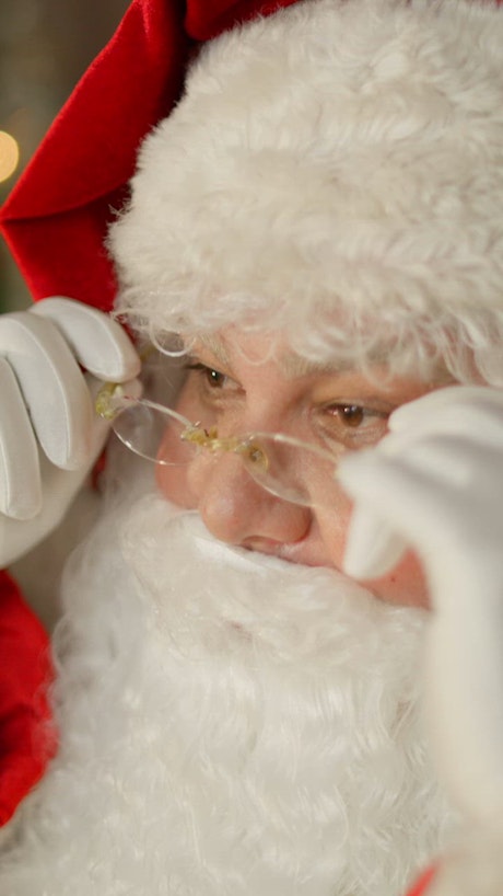 Close up shot of Santa Claus gently fixing his glasses.