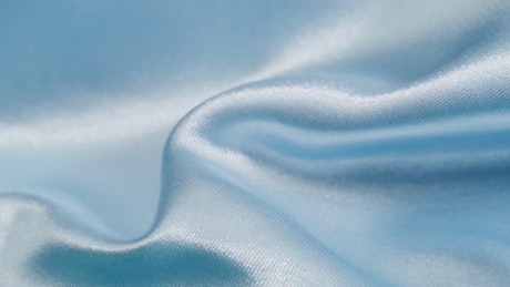 Close up shot of the wrinkles and waves of a satin-textured blue fabric.