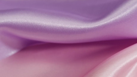Close up shot of the wrinkles and waves of a satin-textured violet and pink fabric.