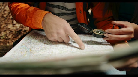 Closeup of hikers using map and compass in forest.