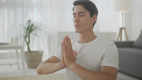 Closeup of man in Namaste yoga pose in living room