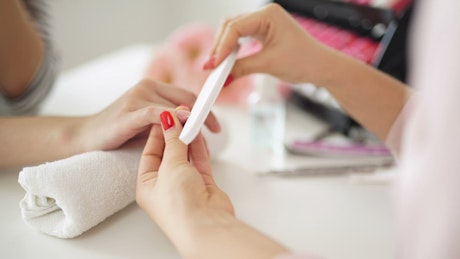 Closeup of manicurist filing woman's nails.