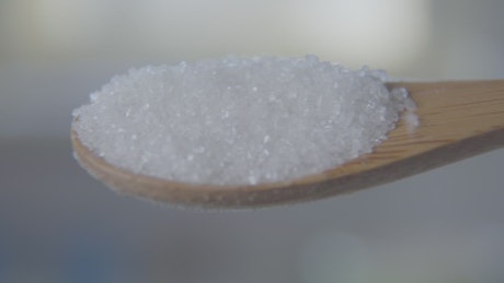 Closeup of sugar spilling from wooden spoon.